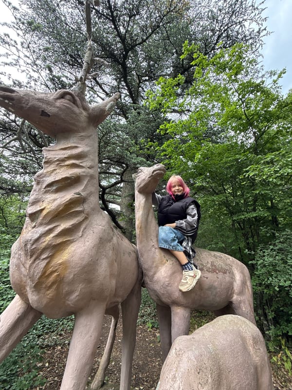 Pink-haired individual explores park, interacts with statues, collects dandelions