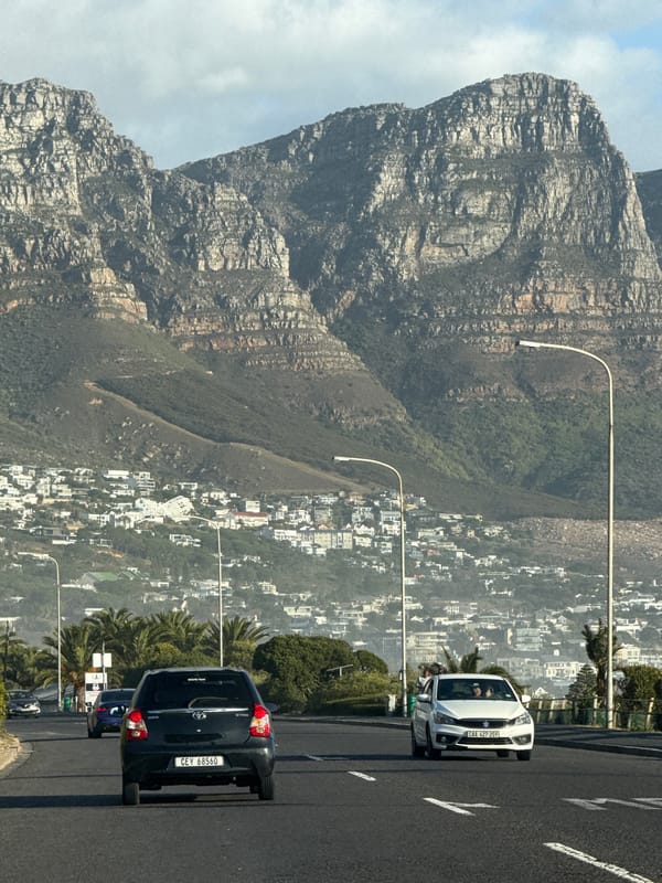 Two cars travel Cape Town road with mountains backdrop