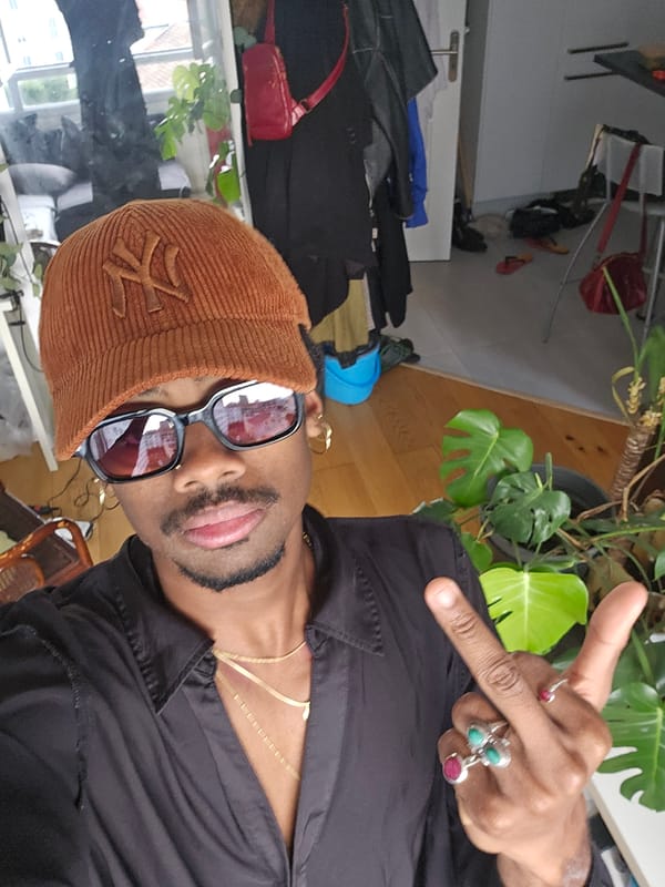 Face-forward in Pantin: cap, shades, gold chains.
