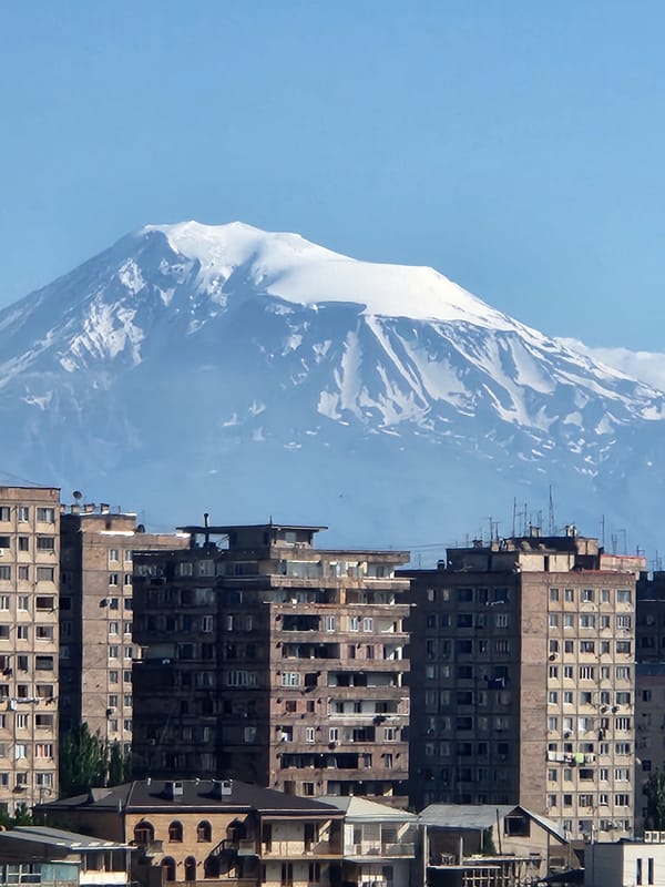 Urban buildings sit in front of a snow-capped mountain range