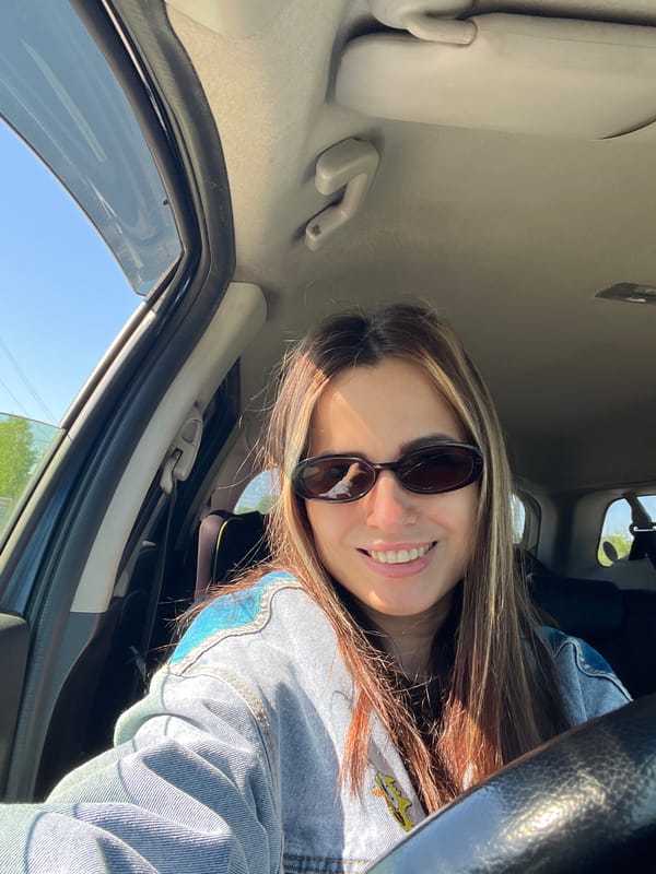 Woman photographed in car wearing denim jacket and sunglasses