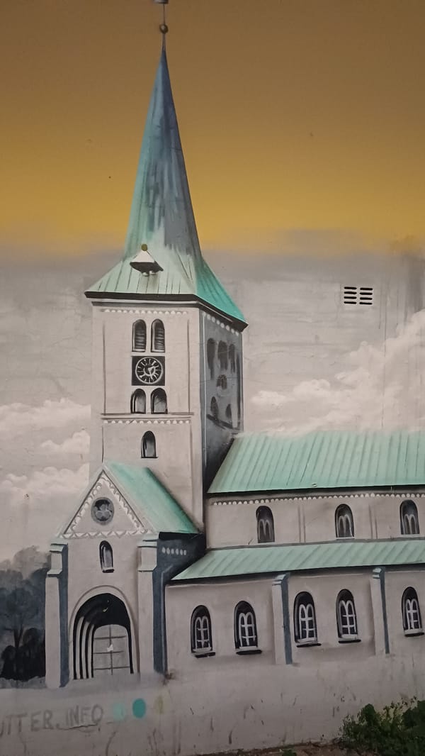 Church plaza at dusk, street lamps on, mural nearby