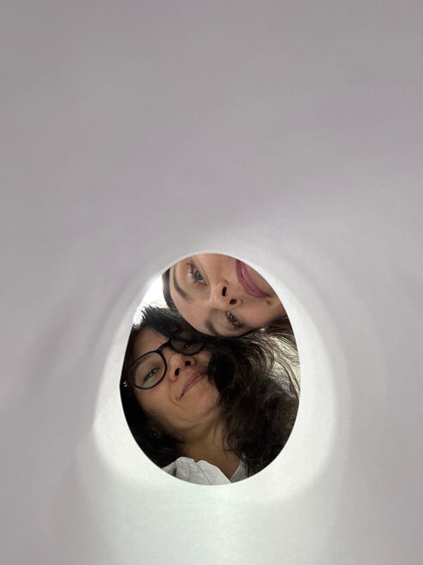 Two people peer through circular opening in white surface