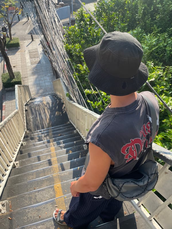 Person in bucket hat observed on concrete stairs in Bangkok