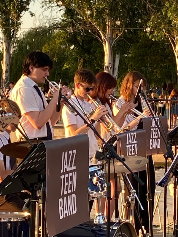 Junior jazz band performs outdoors by the water at sunset