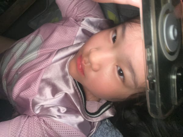 Child with cracked phone rests on bed in pink jersey
