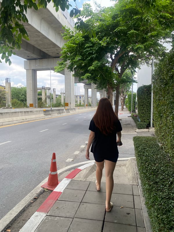 Woman in black dress walks Bangkok sidewalk early morning