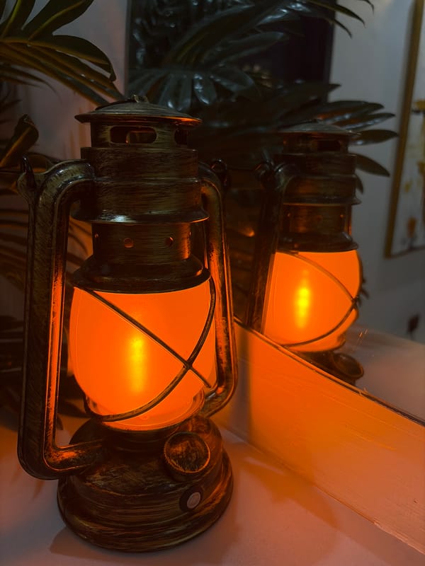Weathered kerosene lantern glowing orange on a reflective surface
