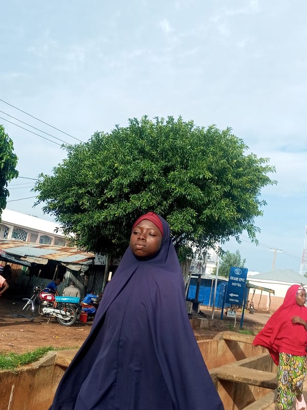 Street scene with lush greenery and a figure in blue hijab