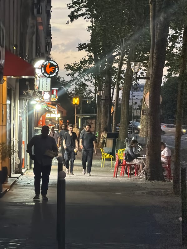 Paris street at dusk: neon signs, sanitation crew, evening crowd