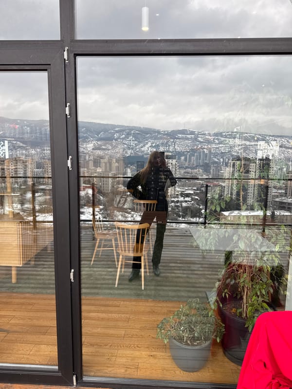 Woman photographs herself on Tbilisi balcony overlooking cityscape