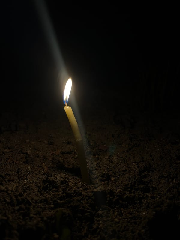Lit candle in red holder placed in dirt during nighttime