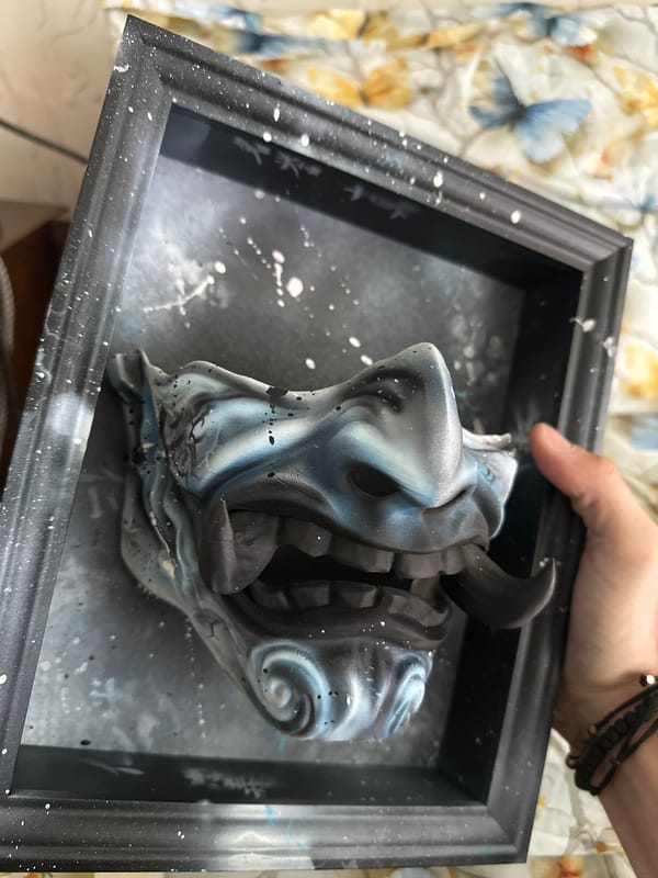 Person displays framed mask artwork with paint splatters in Burgas