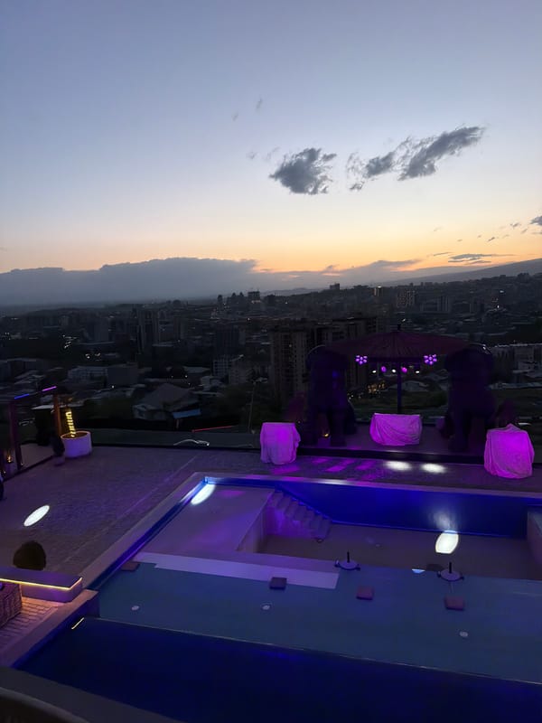 Dusk rooftop pools illuminate against Yerevan skyline amid dramatic clouds