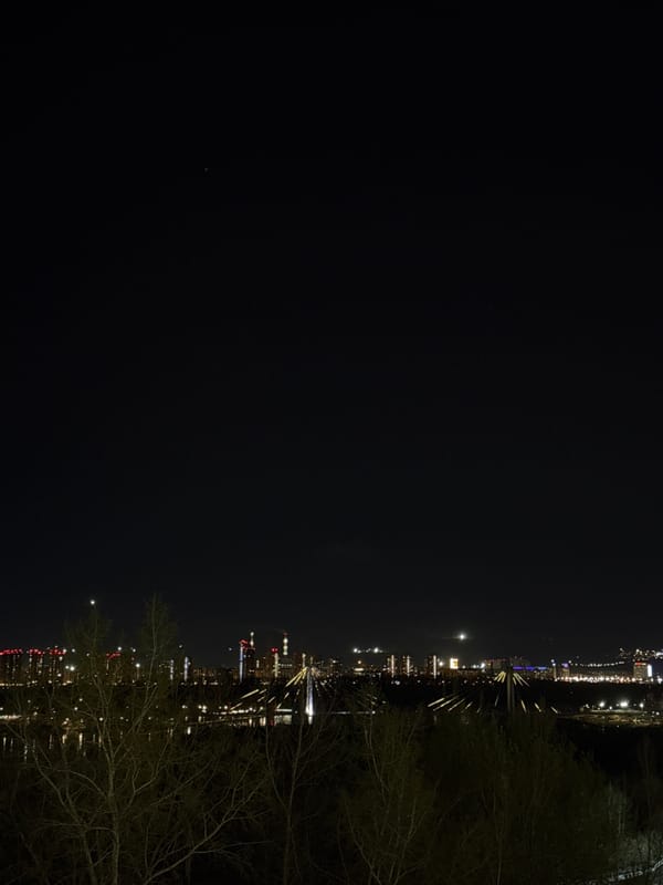 Nighttime cityscape captured in Krasnoyarsk showing illuminated bridge, waterway