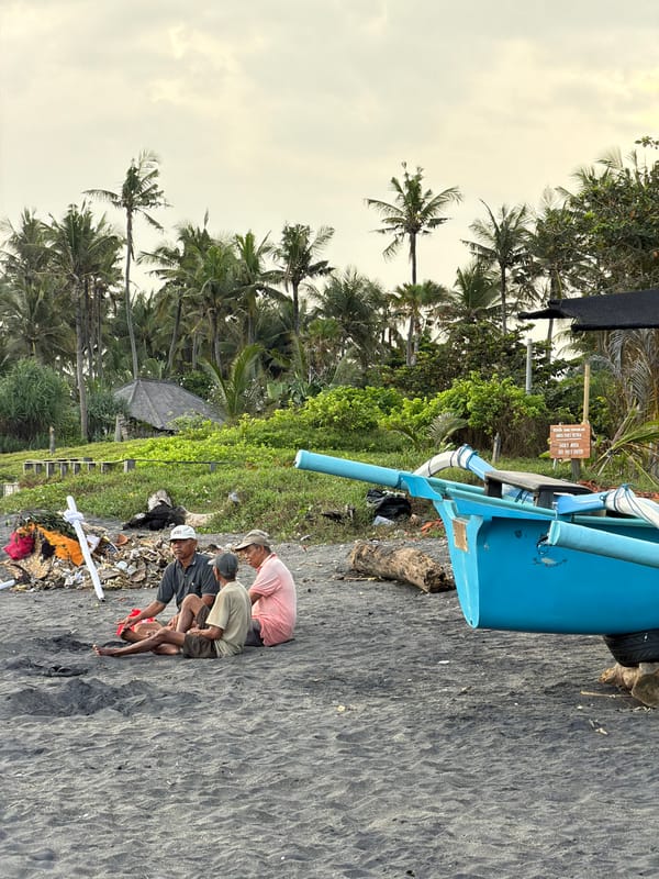 Men gather on beach with outrigger canoe in Mengwi