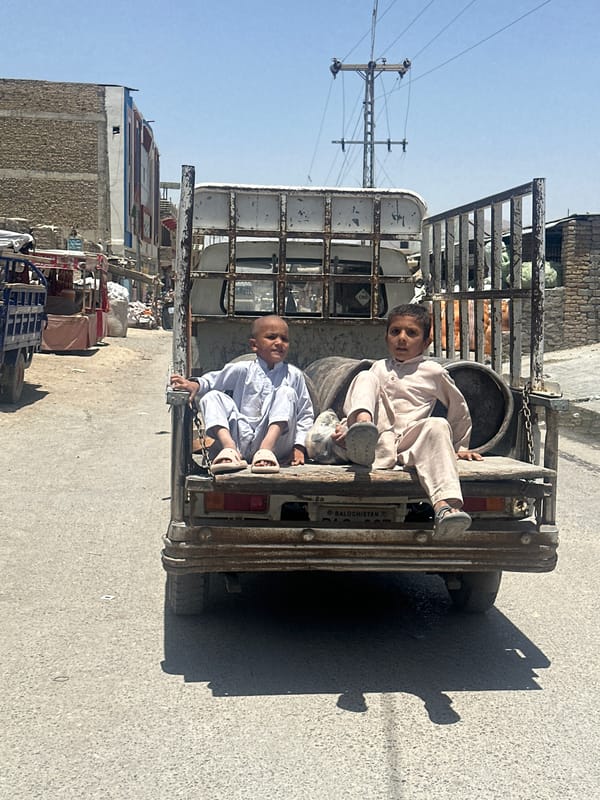 Rusty truck carrying cylindrical cargo through Quetta streets