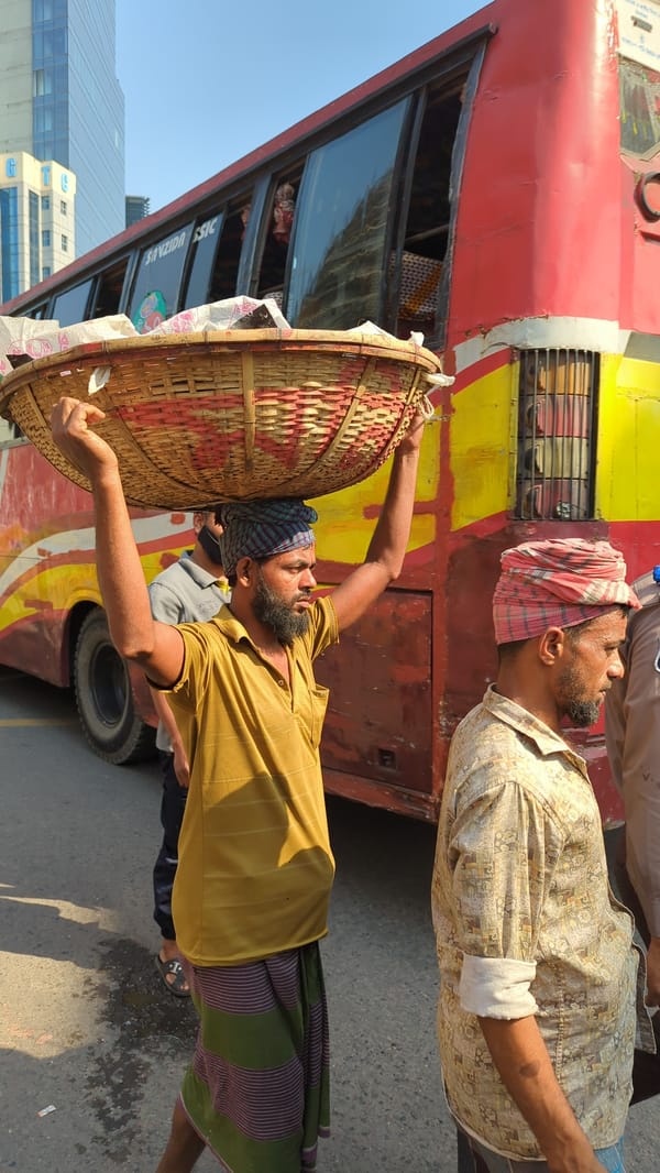 Early morning commuters carry loads near Dhaka bus stops