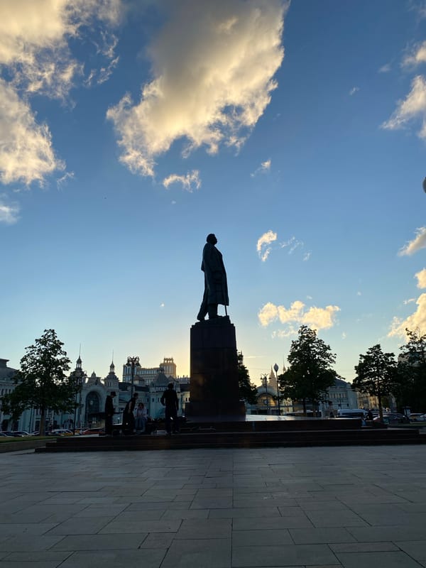 City plaza at dusk: statue, golden light, and a street scene