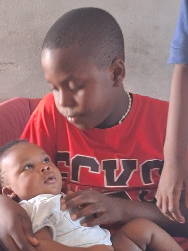 Adult holds baby indoors in Sabon Tasha, Nigeria