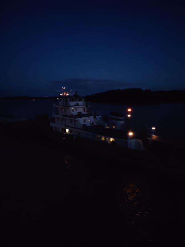Tugboat pushes barge upriver at night near Нова, Russia