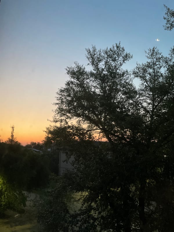 Crescent moon rises over a city street at dusk
