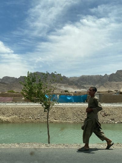 Man walks paved road near canal in Afghanistan