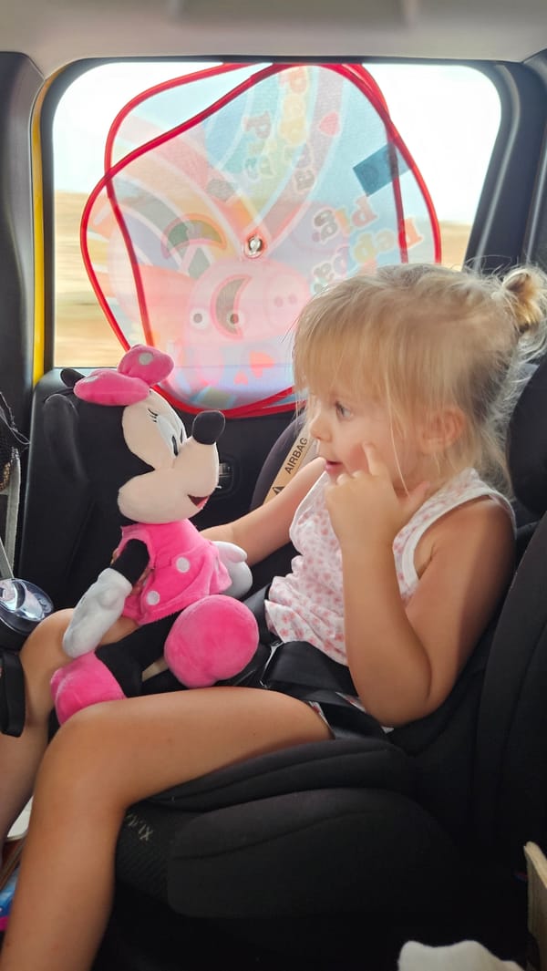 Minnie Mouse plush in hand, pointing from a car seat in Spain