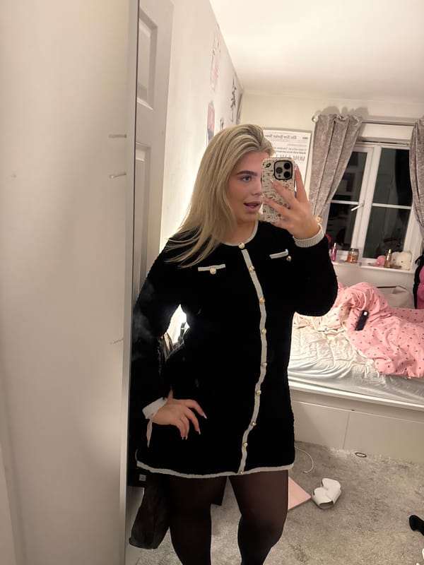 Woman takes mirror selfie in bedroom wearing black dress