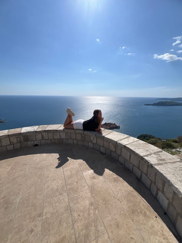 Woman rests on stone wall overlooking Adriatic at Sveti Stefan