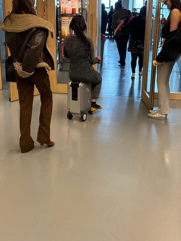 Travelers navigate London building entrance with wheeled luggage