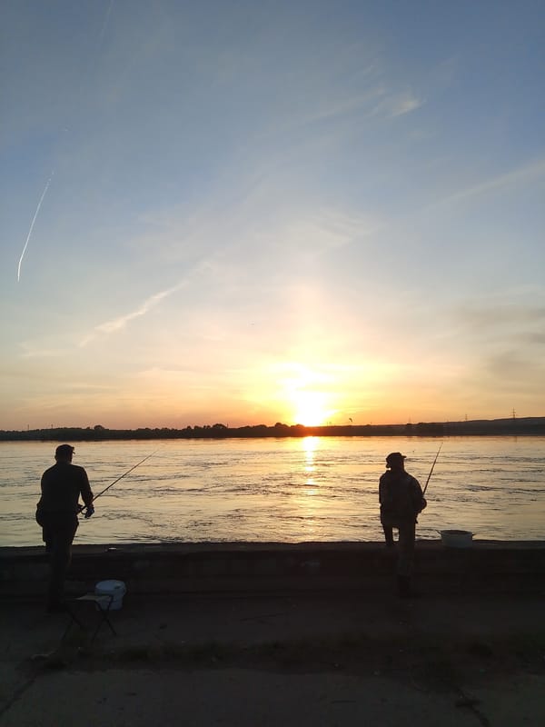 Two anglers fish at sunset on Chaikovsky river embankment