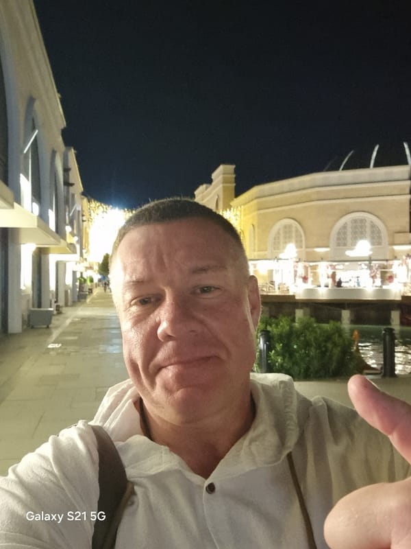 Man poses for nighttime selfie outside illuminated building in Serik