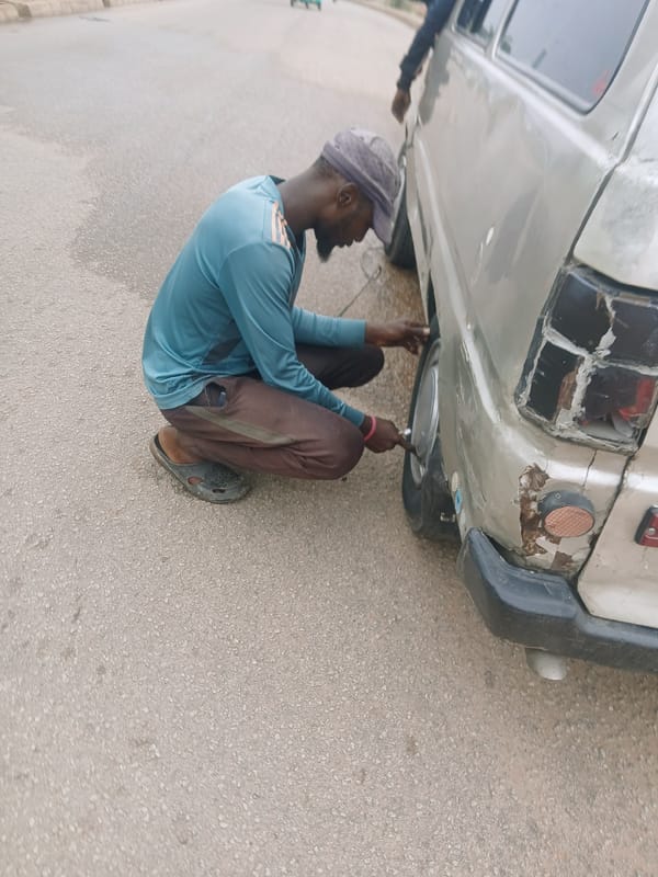 Man performs vehicle maintenance on gray car in Bukuru