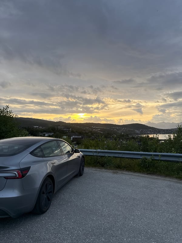 Silver EV parked at sunset overlook above Harstad fjord