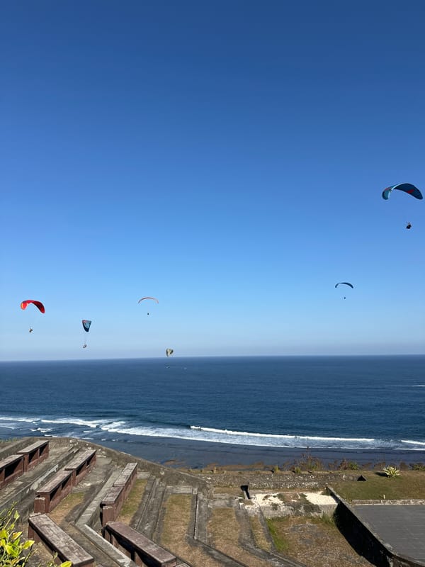 Uluwatu's clifftop amphitheater, cave structure, and paragliders on a clear morning