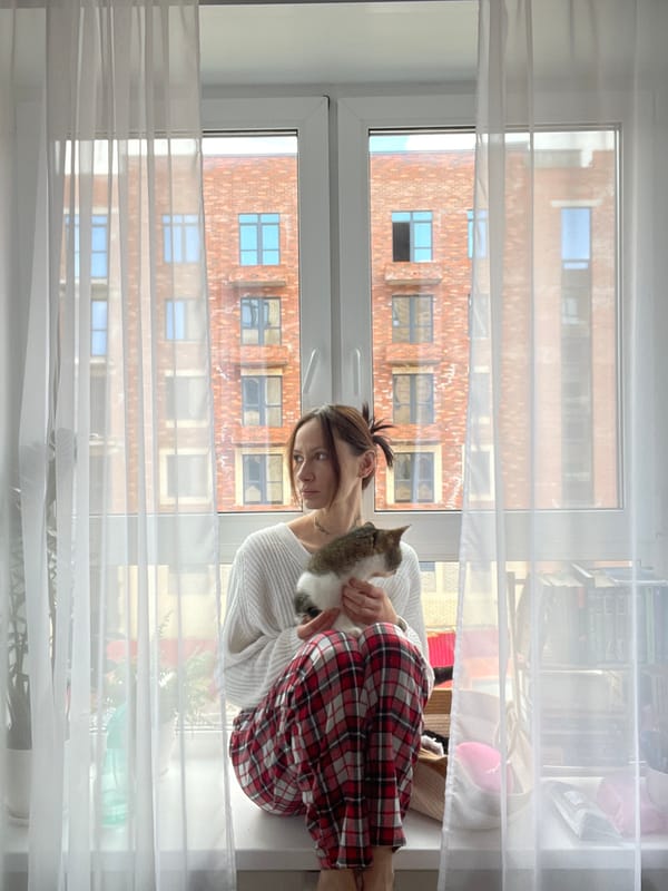 Woman holds cat on window seat in Pervomaysky