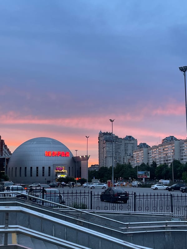 Dusk in a Soviet-era city district, neon Cyrillic signs lit up