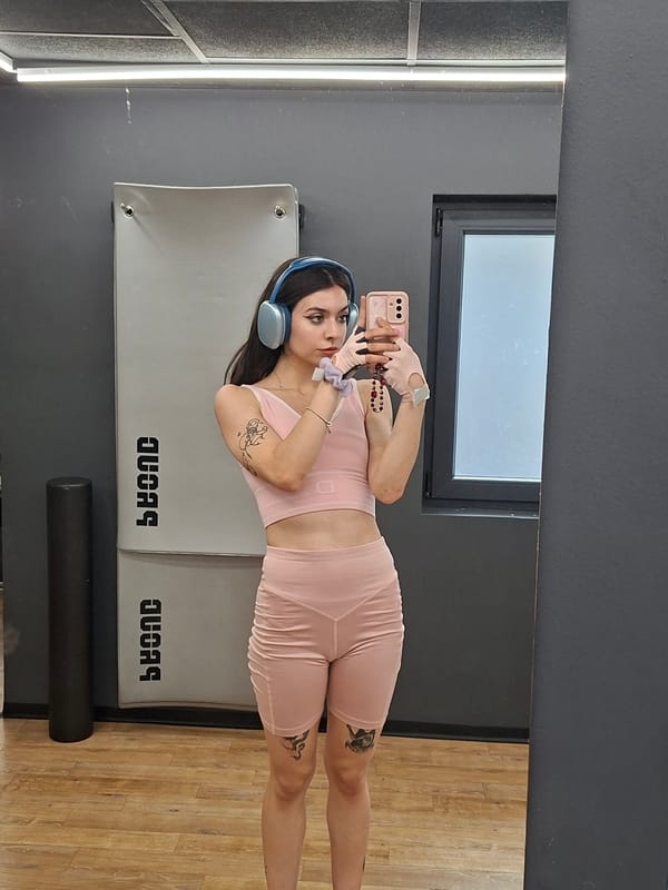 Gym mirror selfie in a pink workout set with blue headphones.