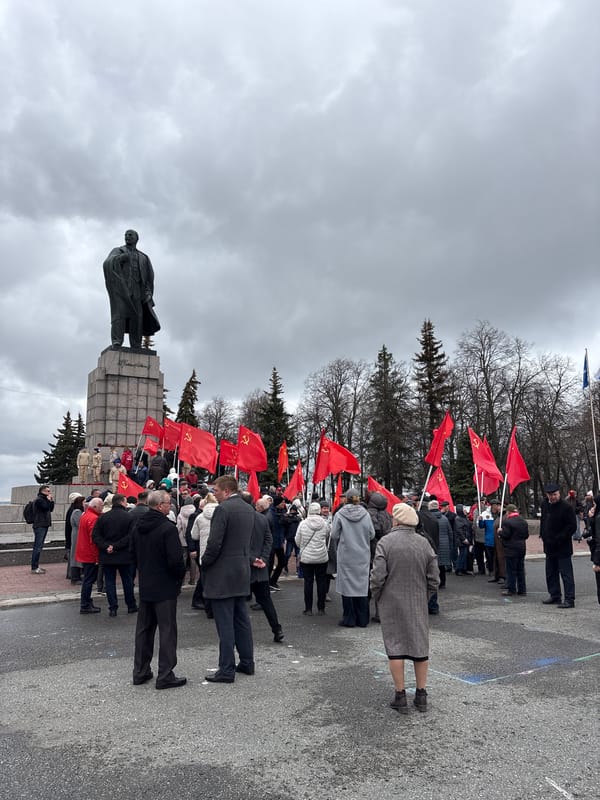 Elderly crowd gathers at Lenin statue with red flags