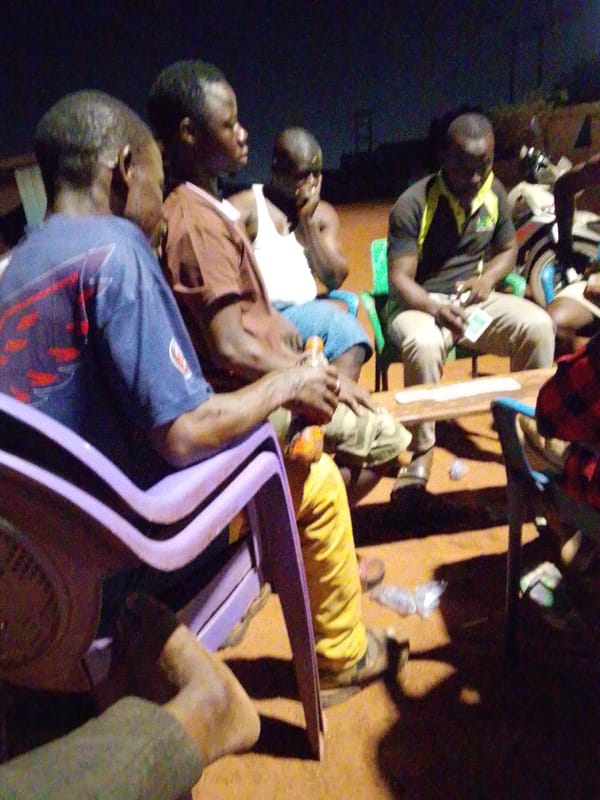 Men gather around table for evening meeting in Tamale