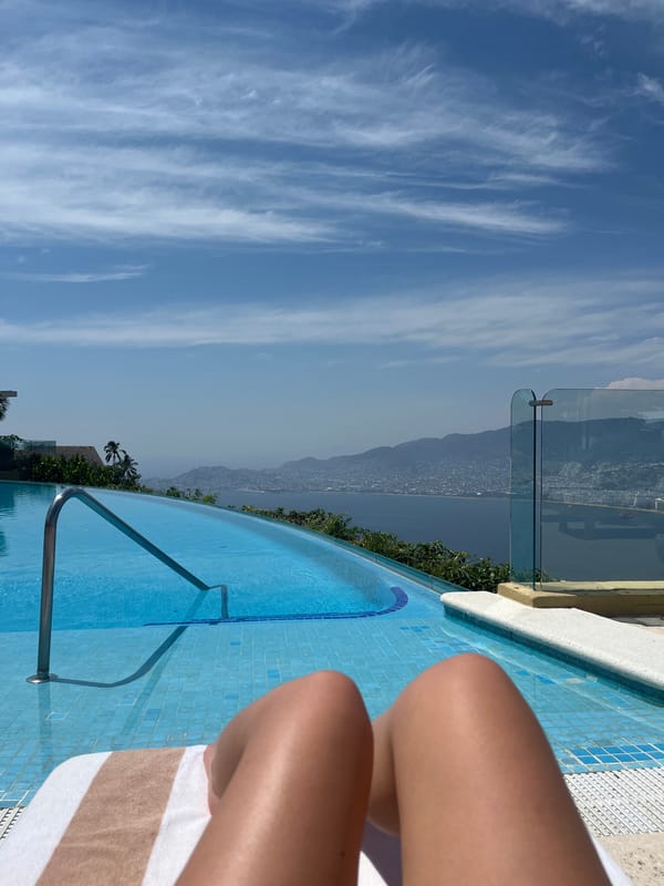 Person relaxes at infinity pool overlooking Acapulco coastline