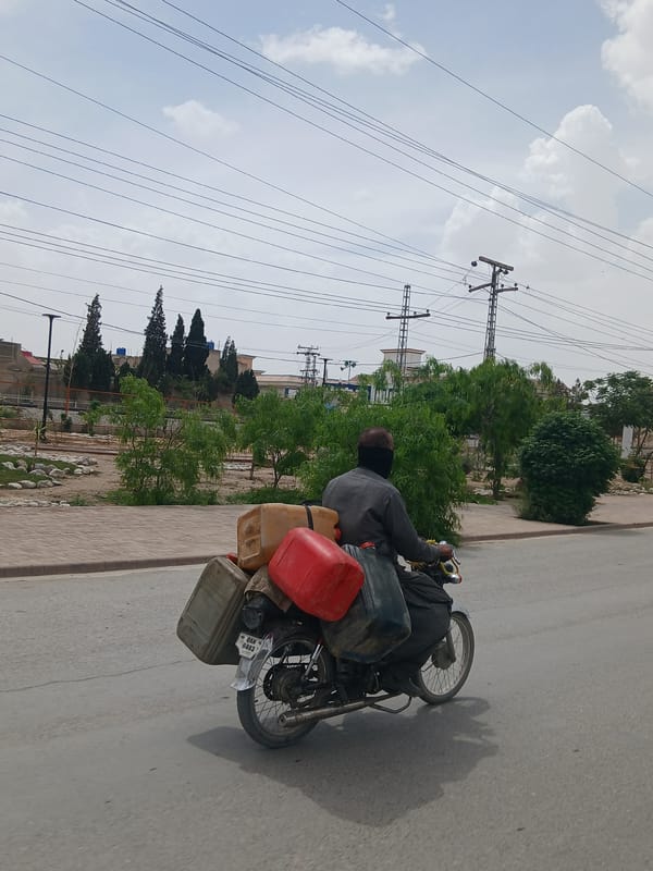 Motorcyclist carries containers on Quetta road beneath power lines