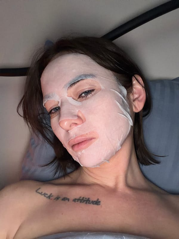 Woman applies facial sheet mask during self-care routine