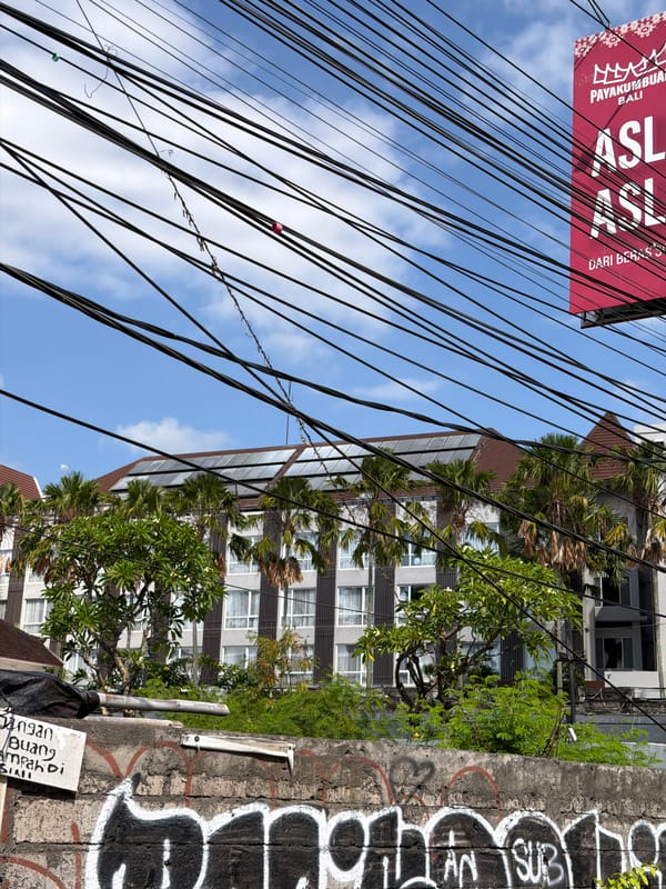 Street-level Kuta: wires, a local carving, and roadside vehicles
