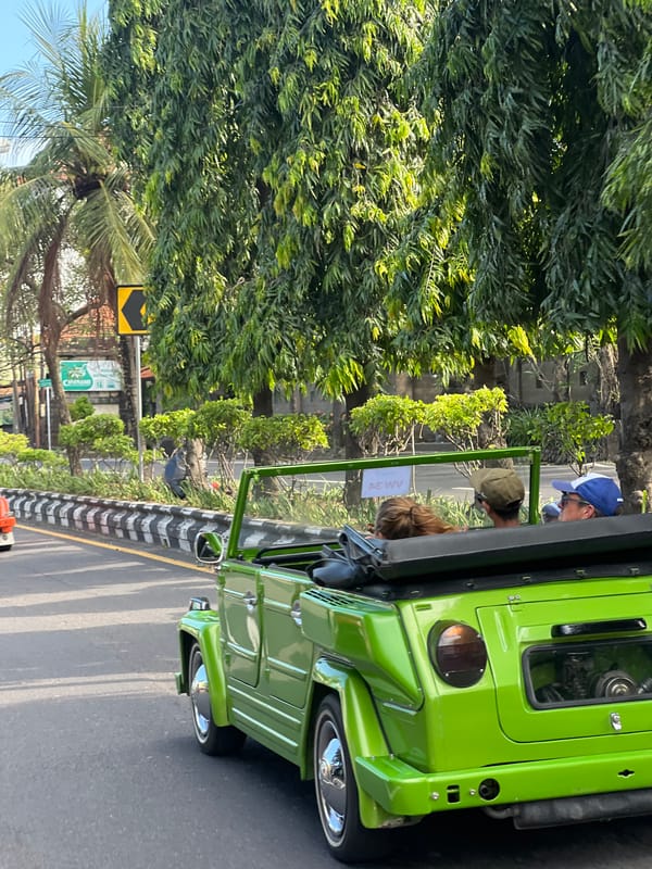 Green Volkswagen carries three passengers through Denpasar streets