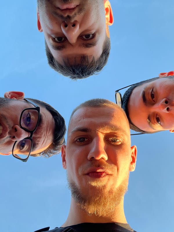 Four men pose in circle formation for upward photo
