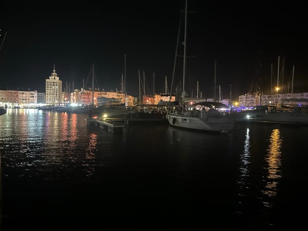 Agde marina at night: Ferris wheel, boats, and a street performer