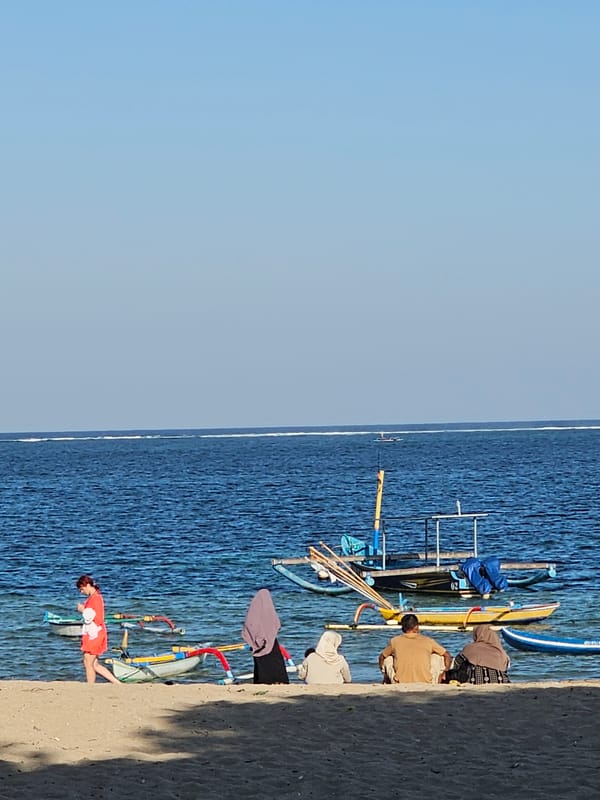 Quiet morning on a Balinese beach with boats and beachgoers