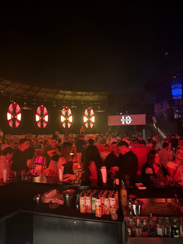 Inside a busy nightclub, red and blue lights, bar crowd
